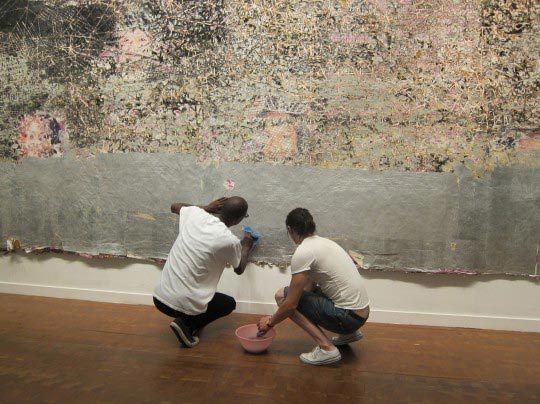 Mark Bradford accompagné de l'un de ses assistants, en train de nettoyer à la main Kingdom Day lors de la Biennale de Séoul en 2010.